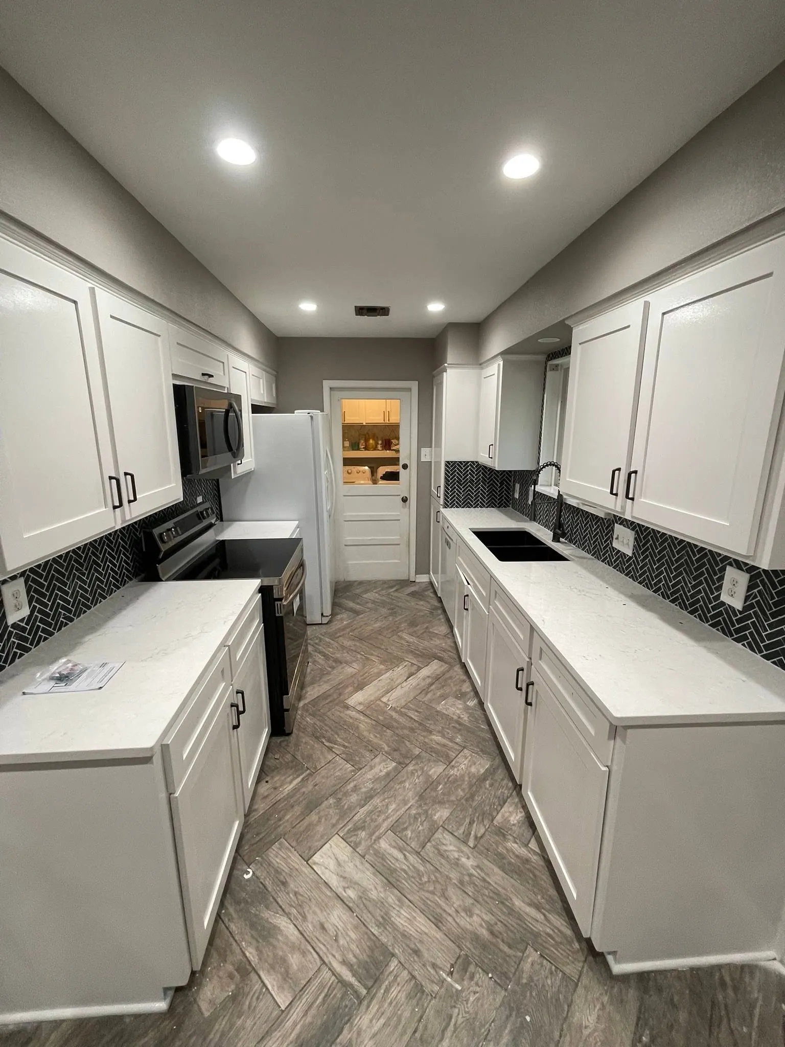 A Corpus Christi galley kitchen remodeled by Nueces Renovations: white cabinets and a black tile backsplash