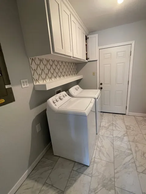 Laundry room with new white cabinets above the washer and dryer and a tile backsplash